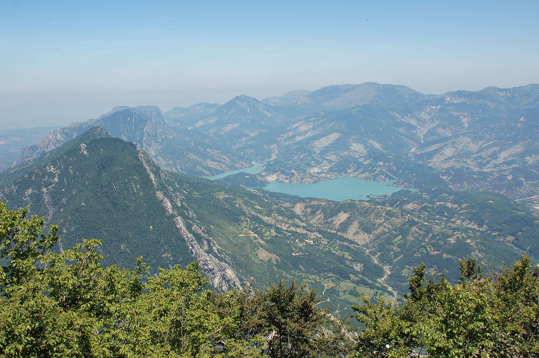 Turquoise Bovilla reservoir from the off-road viewpoint with the Gamti ridge behind